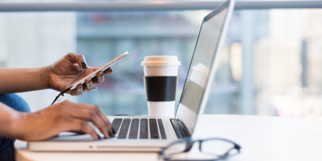 Person bedient Handy und Laptop
