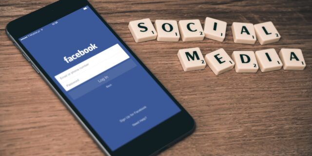 Handy, auf dem Facebook geöffnet ist. Daneben steht Social Media in Scrabble Buchstaben.