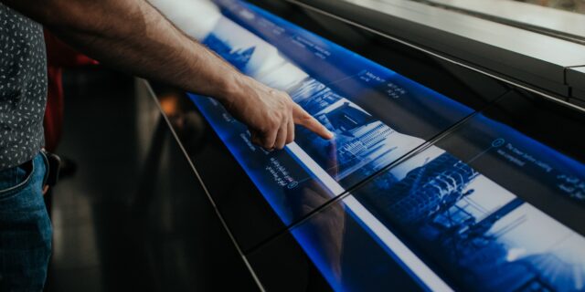 Person hält Finger auf eine Anlage mit Touchscreen