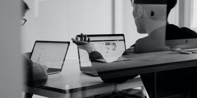 Zwei Personen sitzen an ihren Laptops und diskutieren miteinander.