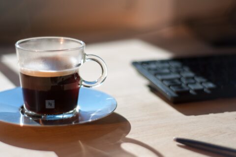 Nespresso Glas, mit Kaffee zu 3/4 gefüllt. Das Glas steht auf einem Holztisch.