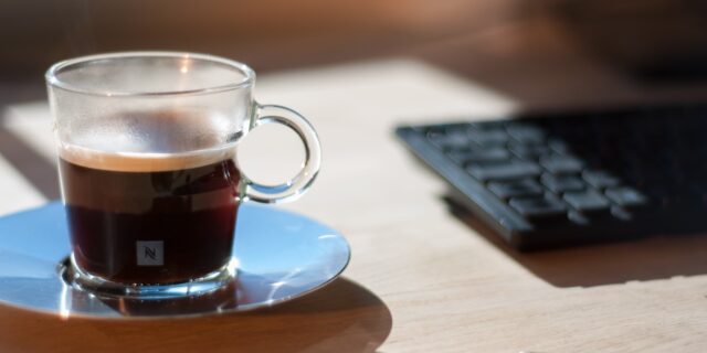 Nespresso Glas, mit Kaffee zu 3/4 gefüllt. Das Glas steht auf einem Holztisch.