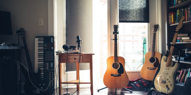 Ein Raum, in den durch ein Fenster Licht fällt. Am Boden stehen ein Keyboard, zwei Gitarren, zwei Bässe und ein Aufnahmegerät.