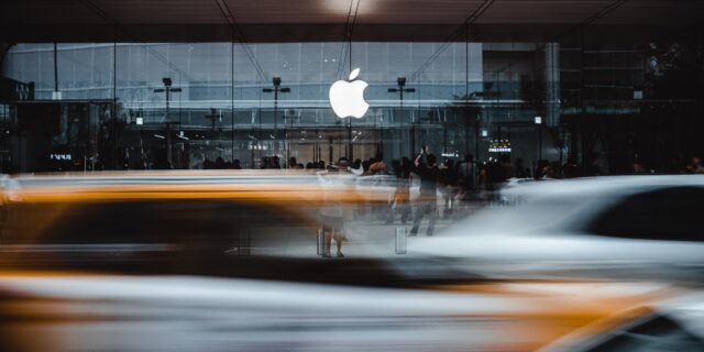 Autos fahren auf einer Strasse, dahinter ist ein Apple Store.