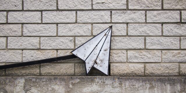 Papierflieger vor weisser Ziegelsteinwand.