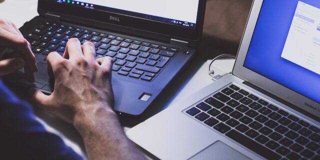 Zwei Laptops nebeneinander, ein DELL Computer und ein MacBook Air. Eine Person bedient den DELL Computer.