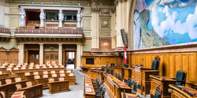 Schweizer Bundeshaus von innen. Tische und Stühle, ein Landschaftsbild an der Wand.