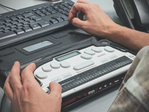 Blick über die Schulter einer Person, die vor einem Laptop mit Tastatur und Braillezeile sitzt