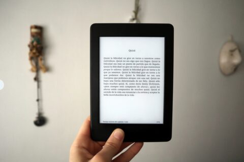 Eine Hand, die ein e-book in der Hand hält. Auf dem Bildschirm ist ein Text auf Spanisch zu lesen. Der Hintergrund des Bildes ist verschwommen zu sehen.