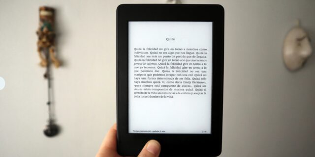 Eine Hand, die ein e-book in der Hand hält. Auf dem Bildschirm ist ein Text auf Spanisch zu lesen. Der Hintergrund des Bildes ist verschwommen zu sehen.