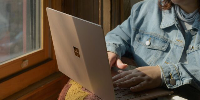 Junge Frau mit Microsoft Surface auf dem Schoss sitzt am Fenster.