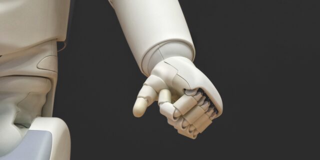 Weisse Roboterhand zu einer Faust geballt vor schwarzem Hintergrund