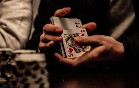 Die Hände einer Person, die gerade Pokerkarten mischt. Im Vordergrund stehen aufgestapelte Poker Chips
