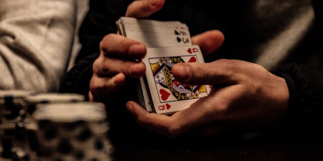 Die Hände einer Person, die gerade Pokerkarten mischt. Im Vordergrund stehen aufgestapelte Poker Chips