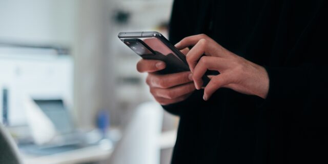 Person hält Smartphone in der Hand und hält den Zeigefinger auf dem Bildschirm.