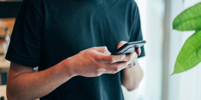 Ein Mann hält ein Smartphone in den Händen, die Daumen sind auf dem Bildschirm.