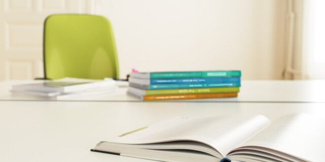 Tisch mit aufgeschlagenem Lehrmittel, weitere aufgestapelte Bücher im Hintergrund auf dem Tisch