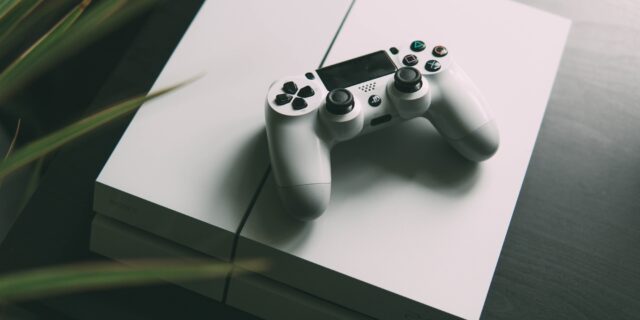 PS4 auf einer Box am Boden. Eine dekorative Pflanze steht daneben.