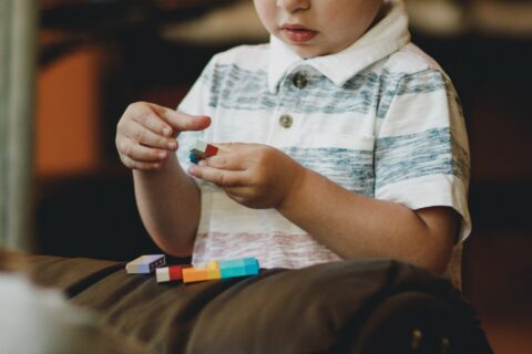Kleinkind setzt LEGO-Bauteile zusammen, man sieht seinen Oberkörper und sein Gesicht bis zur Nase
