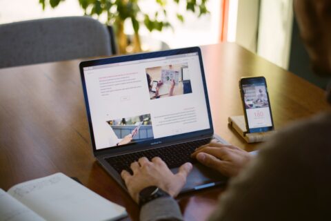 Hände einer Person über der Tastatur eines Laptops. Auf dem Bildschirm ist eine Webseite zu sehen.