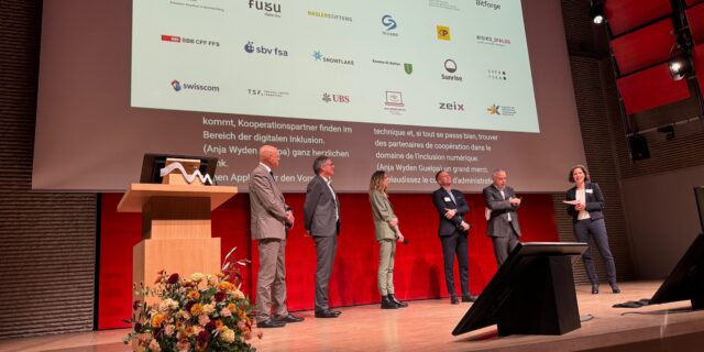 Sechs elegant gekleidete Personen auf einer Bühne, dahinter eine Leinwand mit den Logos der ADIS-Gründungsmitglieder